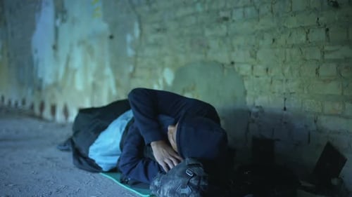 Person Lying in Sleeping Bag Against Brick Wall