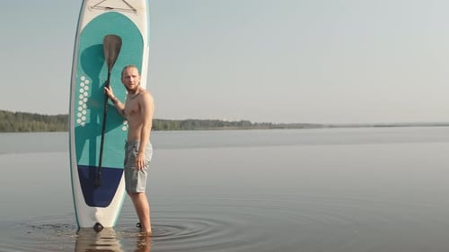Man Holds Paddle Board in Calm Lake Water
