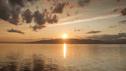Serene Sunset Over Calm Water with Mountain Backdrop
