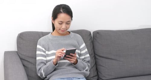 Young Woman Using Smartphone on a Gray Couch