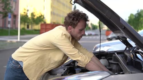 Man Repairs Car Engine in Urban Setting