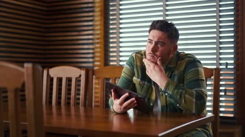 Man Thoughtfully Holding Tablet at Wooden Table