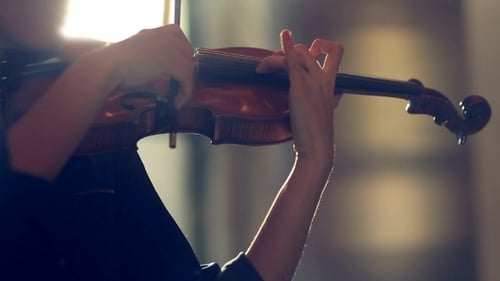 Young adult playing violin in a bright room