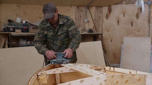 Adult sanding wooden boat frame in carpentry workshop