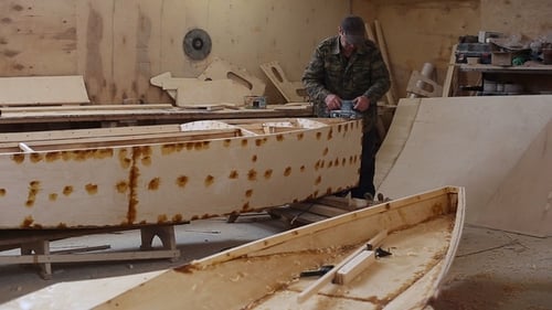 Um carpinteiro lustra detalhes do barco de madeira no estaleiro