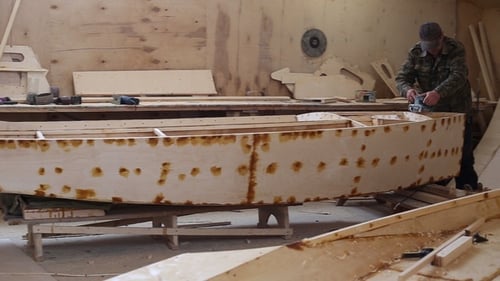 Um carpinteiro lustra detalhes do barco de madeira no estaleiro