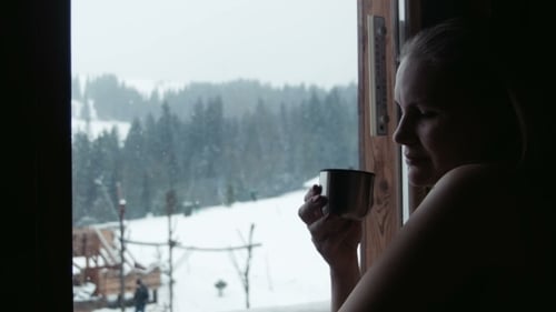 Female Has Tea Near a Window In Winter In Resort