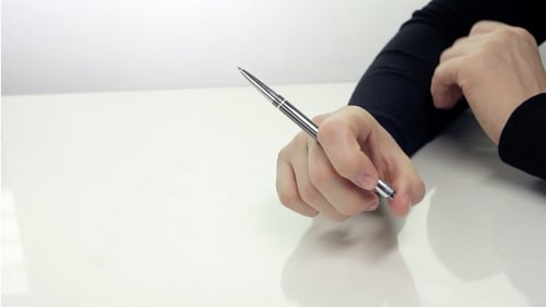 Hand Twirling Pen over White Table
