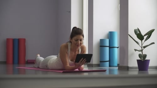 Woman Lies on Yoga Mat Using Tablet