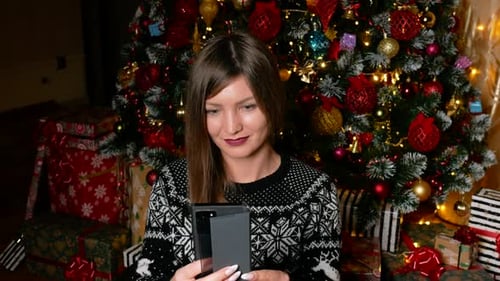 Woman Using Phone by Christmas Tree and Gifts