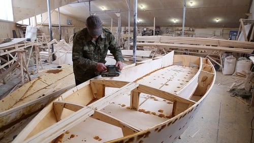 Um carpinteiro lustra detalhes do barco de madeira no estaleiro