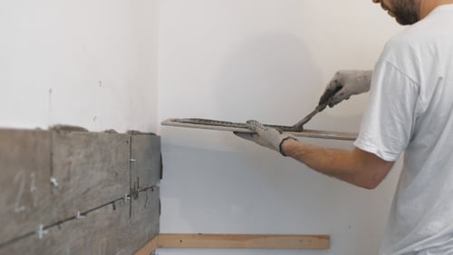 Man Applying Adhesive to Grey Tile in Room