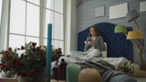 Woman Using Smartphone Sitting on Bed Indoors