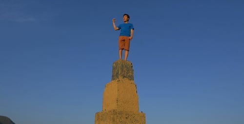 Young Adult Stands on Ancient Stone Pillar Outdoors