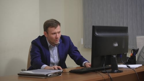 Young Businessman Working In Office, Sitting At Desk, Looking At Computer Screen.
