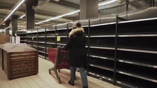 Woman in Warm Jacket Hat Walks with Cart Past Empty Shelves in Russian Store
