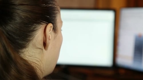 Woman Looking at Dual Computer Screens at Home