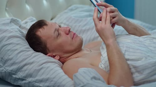 Man Using Smartphone Lying in Bed at Home