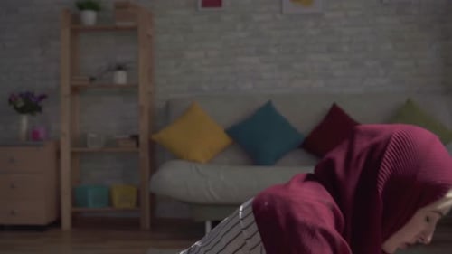 Muslim Woman in a Traditional Scarf Praying on Rug in Her Living Room Close Up
