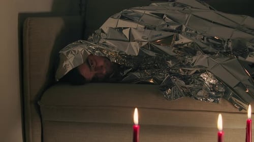 Homme couvert d'une couverture en aluminium regardant des bougies