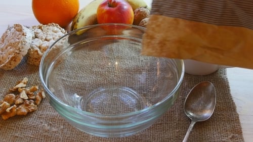 Pouring Cornflakes into Bowl with Fruit for Breakfast