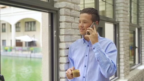 Young Man Talking on Phone with Coffee by Window
