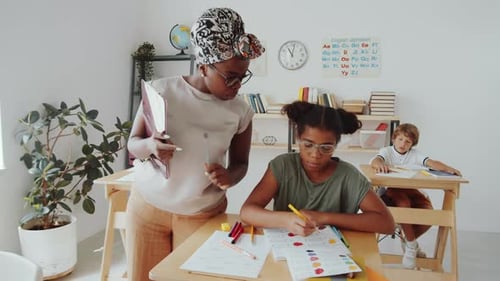Afro-American Teacher Helping Children during Lesson in Primary School