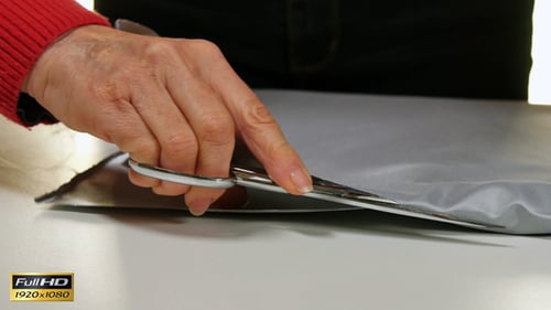 Person Cutting Gray Fabric with Scissors