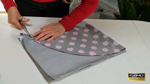 Cutting Gray Fabric with Scissors on a Table