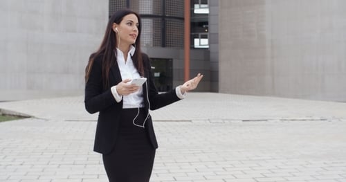 Woman Using Smartphone with Earbuds Outside Building