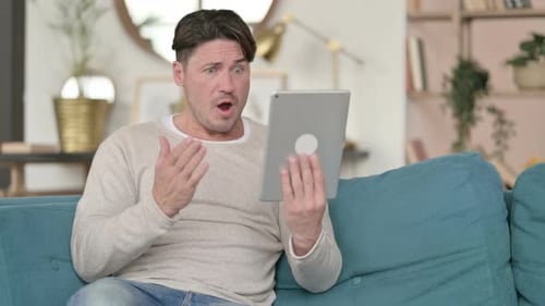 Man Talks on Tablet While Sitting on Couch