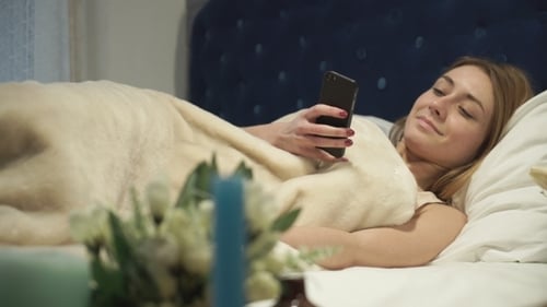 Woman Lies in Bed Texting on Mobile Phone