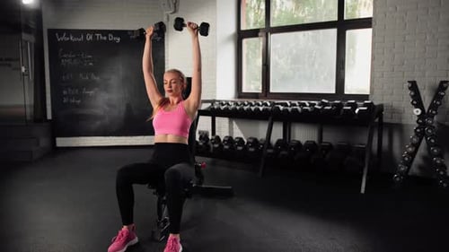 The girl does an exercise in the gym. Female athletic woman exercising shoulders with dumbbells