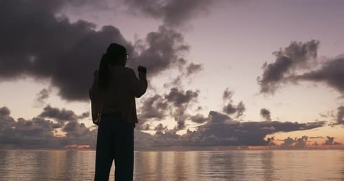 Silhouette einer Frau, die bei Sonnenaufgang die Hand hebt