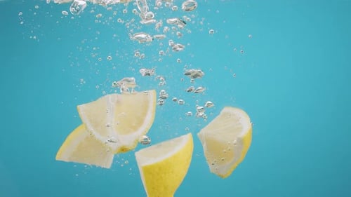 Lemon Wedges Splashing into Water on Bright Background