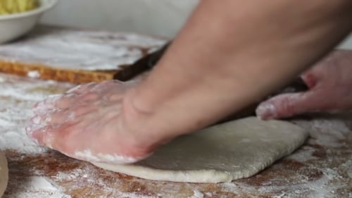 Hands Flattening Dough with Rolling Pin on Wood