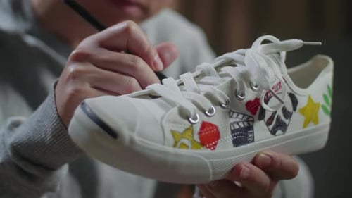 Close Up Of Male Footwear Designer's Hands Putting Coloured Unique Patterns On Sneakers At Home