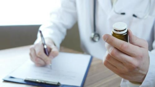 Doctor Writing a Prescription While Holding Medication