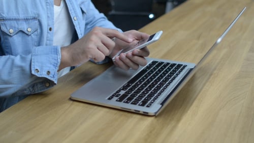 Person Using Phone with Laptop on Desk
