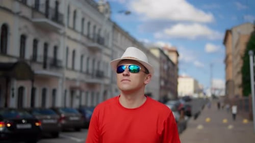 A Young Man in a Hat Walks Around the City Examines the Buildings Around Camera Movement