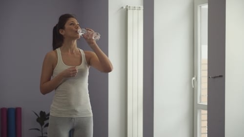 Woman Drinks Water From a Bottle In a Gym