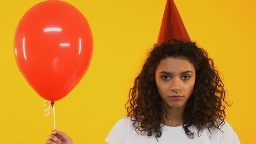 Woman in Party Hat Holds Red Balloon, Looks Sad
