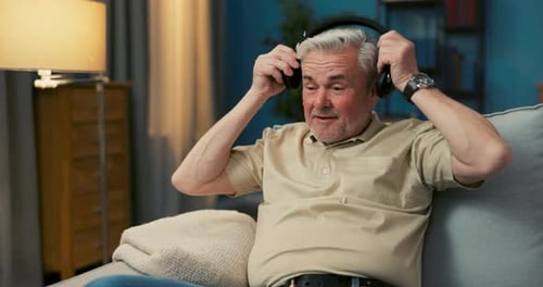 Man Listens to Music with Wireless Headphones at Home