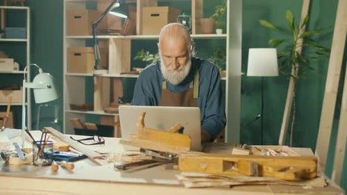Senior Man with Laptop in Carpentry Workshop