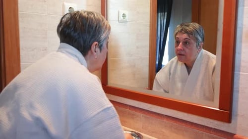 Woman Applies Lotion to Face in Bathroom Mirror