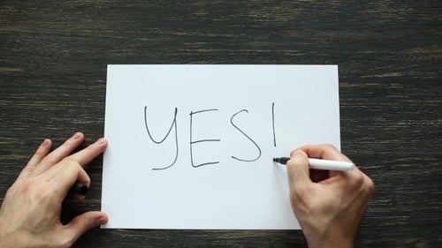 Man Hand Writing Yes With Black Marker On White Paper. Top View