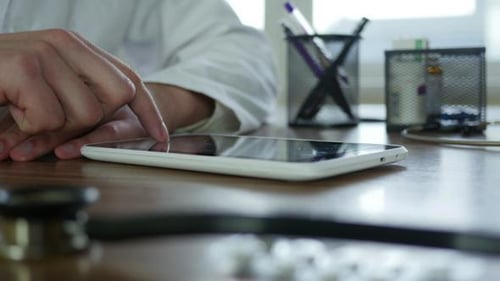 Doctor Using Tablet in Office with Medical Equipment