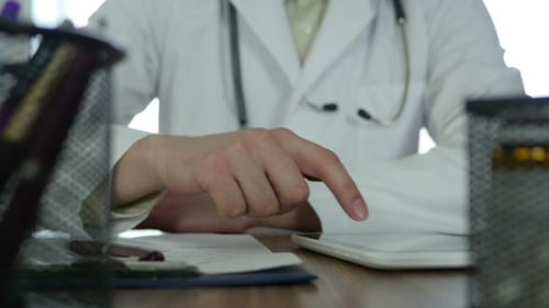 Doctor Using Tablet and Writing Notes at Desk