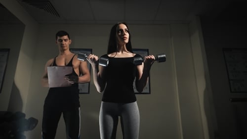 Trainer Men Are Teaching Woman Lifting a Dumbbell