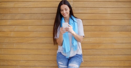 Woman Texting While Leaning Against Wall